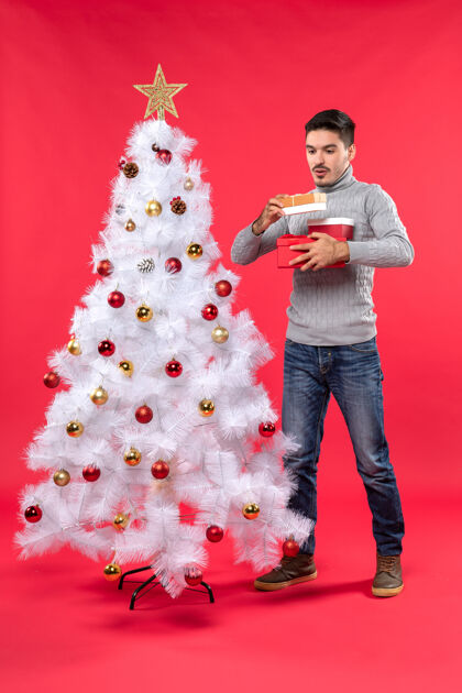 圣诞树站在装饰过的白色圣诞树旁的穿着灰色上衣的帅哥大人的俯视图服装圣诞礼物