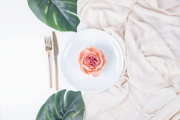 装饰一朵玫瑰放在白色的盘子里 上面有假叶子和桌布叶桌布顶视图