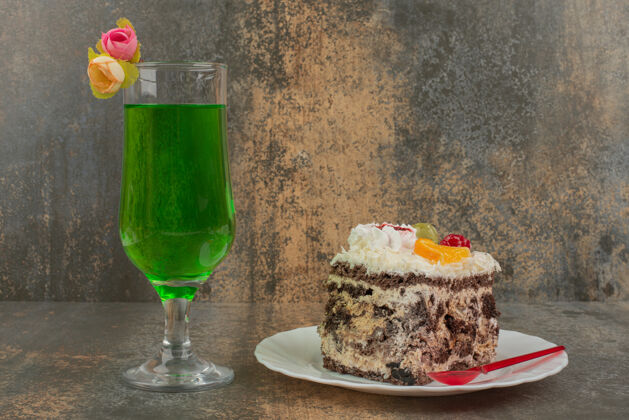 勺子在大理石墙上放一块蛋糕和一杯多汁的绿色柠檬水玻璃杯柠檬水饮料
