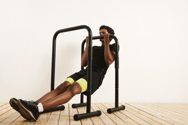 器械肌肉发达的非洲裔美国运动员 穿着黑色运动服 靠着白墙和轻质木地板 在移动吧台上做体重排肌肉健美肌肉
