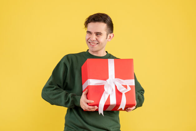 人正面图：穿着绿色毛衣的快乐年轻人拿着黄色的圣诞礼物快乐的年轻人男人肖像
