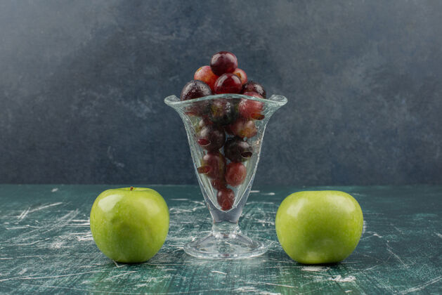湿的湿苹果和一杯黑葡萄放在大理石桌上苹果有机完整的