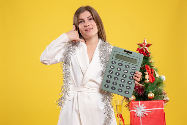 女性正面图女医生站着拿着计算器 背景是黄色的圣诞树和礼品盒站着成人人物