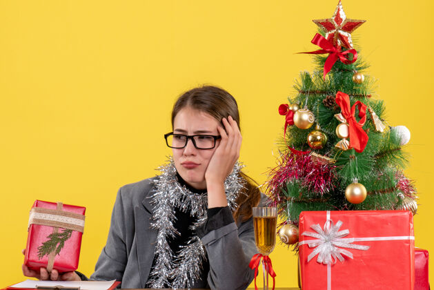 肖像前视图体贴的女孩戴着眼镜坐在桌旁圣诞树和鸡尾酒礼物漂亮花束鸡尾酒