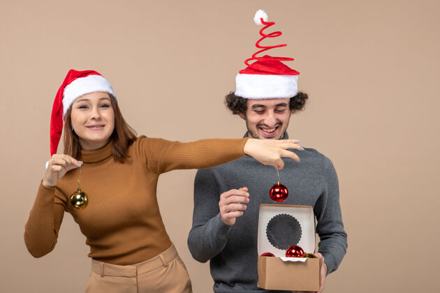 圣诞节喜庆的心情带着兴奋可爱的情侣戴着红色圣诞老人帽打开装饰饰品上的灰色配件男人节日
