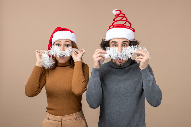 节日新年心情喜庆的概念与兴奋酷满意可爱的情侣戴着灰色股票上的红色圣诞老人帽的形象男人面具心情