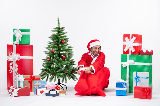 坐着圣诞老人坐在地上 拿着圣诞袜 靠近礼物和装饰过的圣诞树礼物礼物圣诞树