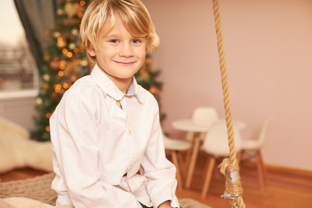 孩子穿着白衬衫的可爱欧洲男孩的肖像 享受着节日的气氛 期待着平安夜 坐在装饰着新年树的客厅里 开心地微笑着孩子肖像微笑