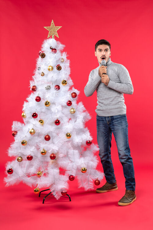 心情新年心情与困惑积极的家伙穿着牛仔裤站在装饰圣诞树附近的红色站着帽子圣诞树