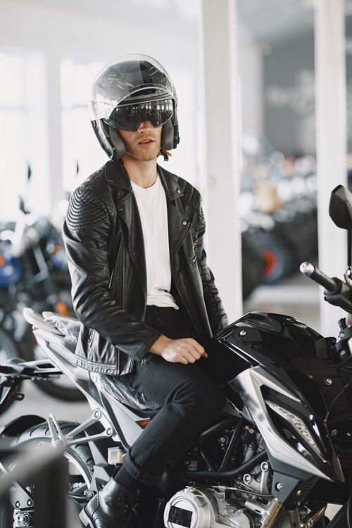 阳刚一个男人在摩托店里选摩托车一个穿黑夹克的男人一个戴头盔的男人车辆摩托车手阳刚