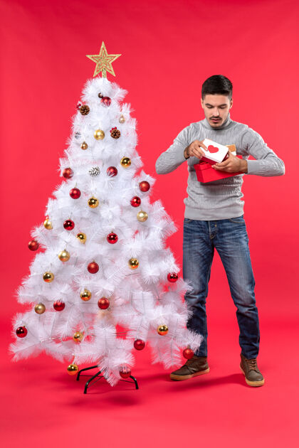 圣诞树站在装饰过的白色圣诞树旁的穿着灰色上衣的年轻人的俯视图年轻成人肖像衬衫