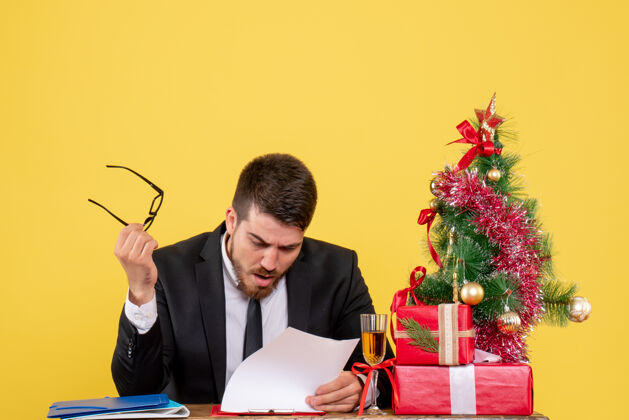 公司正面图：一位男性工人在他的桌子后面 黄色的圣诞树上放着礼物和圣诞树年份圣诞工人