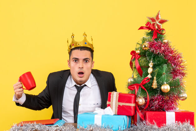 套装正面图大眼睛男人拿着皇冠拿着杯子坐在圣诞树和礼物旁边礼物成人树
