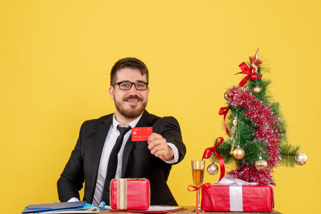 银行正面图：坐在工作场所后面的男工人拿着黄色的银行卡圣诞节新郎男