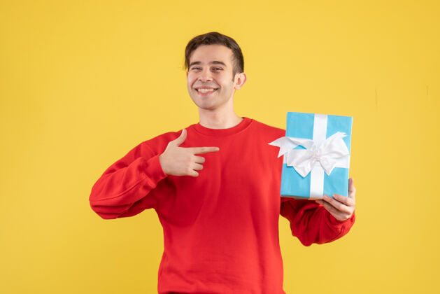 人物正面图幸福的年轻人穿着红色毛衣指着黄色的礼物男士帅气运动衫