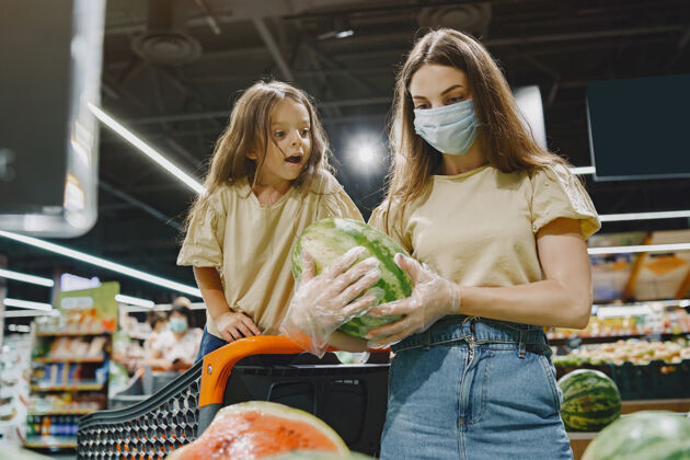女人一家人在超市戴着防护面具的女人人们选择蔬菜母亲带着女儿冠状病毒杂货店Covid19购物狂
