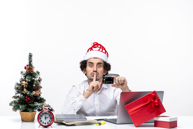 沉默一个戴着圣诞老人帽子 拿着银行卡的商人惊讶地在办公室里做着沉默的手势手势卡片人