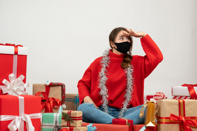 女孩穿着红色毛衣的年轻女孩看着坐在周围的东西 白色的面具上戴着黑色的礼物人们礼物年轻人