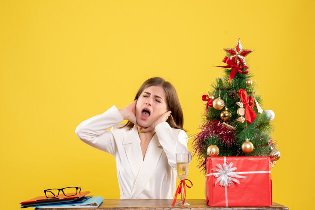 前面正面图：女医生坐在黄色背景的桌子前 放着圣诞树和礼品盒办公室坐女医生
