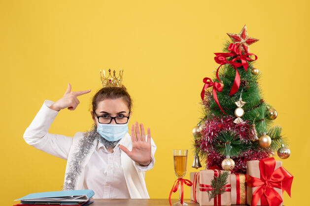 背景正面图女医生戴着黄色背景的无菌口罩坐在圣诞树和礼盒里情感坐着颈部