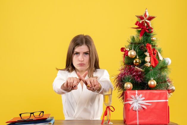 快乐正面图：女医生坐在黄色背景的桌子前 放着圣诞树和礼品盒导演女性医生