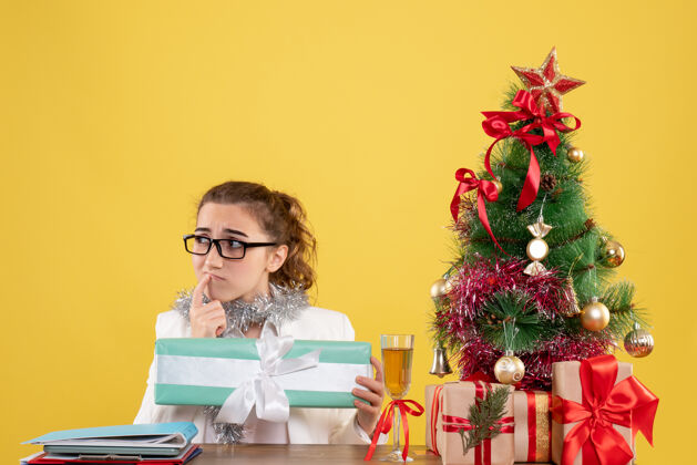 女性正面图女医生围坐在圣诞礼物和黄色背景上拿着礼物的树上周围圣诞树人