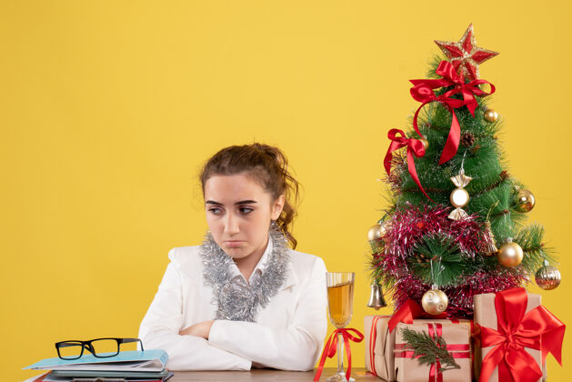 坐着前视图女医生围坐在圣诞礼物和圣诞树周围 在黄色背景下感到悲伤树感觉背景