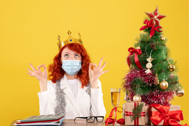 树前视图：女医生带着圣诞礼物坐着 戴着黄色背景的皇冠前面坐礼物