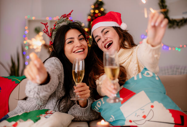 坐着快乐的年轻女孩戴着圣诞帽 手拿香槟和火花杯 坐在扶手椅上 在家里享受圣诞节时光年轻眼镜家