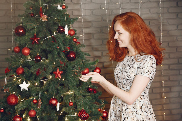 红发圣诞树旁的优雅女士家里拿着香槟的女士乐趣圣诞树室内