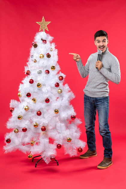 站着新年气氛积极的家伙穿着牛仔裤站在装饰圣诞树附近心情指向圣诞树