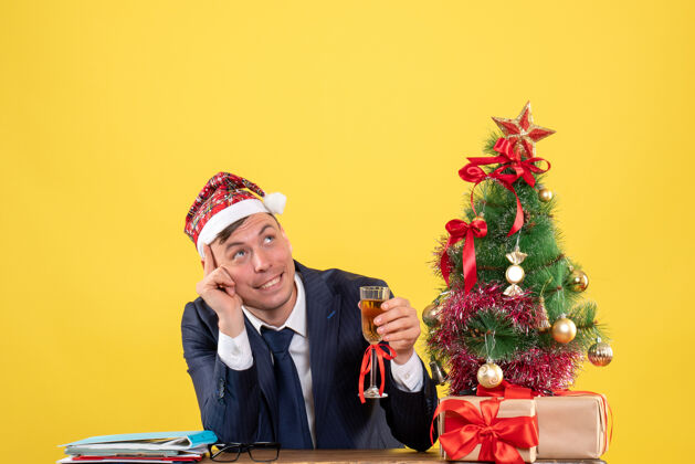 男人商务人士坐在圣诞树旁的桌子旁敬酒 黄色的礼物职业公司圣诞节