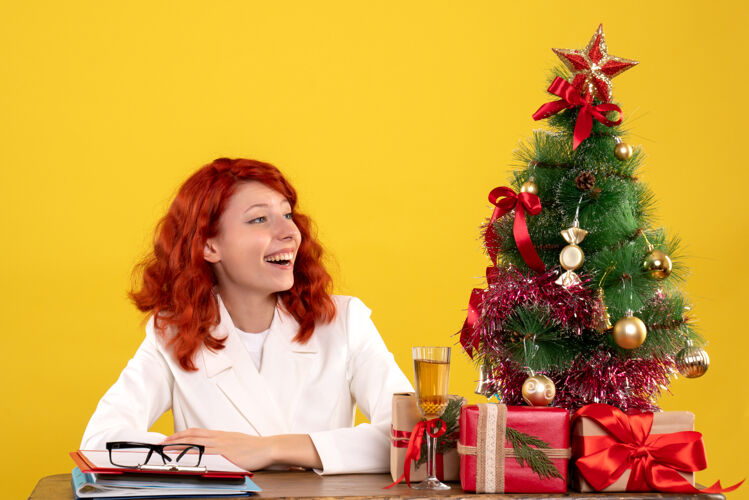 成人女工人坐在桌子后面 手里拿着圣诞礼物和黄色的圣诞树女黄色主任