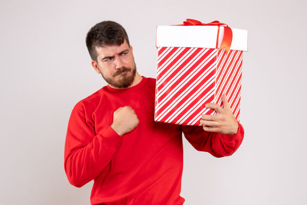 人身穿红衫的年轻人在白色墙上的盒子里拿着圣诞礼物肖像盒子前面