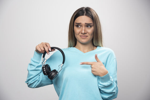 成人穿着蓝色运动衫的金发女孩听着耳机 不喜欢音乐Dj服装摆姿势