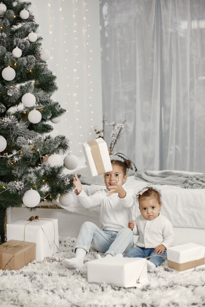 盒子穿着白色毛衣的孩子女儿们在圣诞树旁缝线两个姐妹在家女儿儿童灯