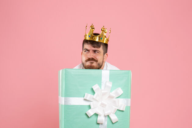 聚会年轻人在礼物盒内的正面视图 浅粉色墙上有皇冠丝带里面男人