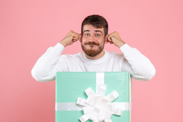 正面礼物盒内的年轻人在粉色墙上做鬼脸的正面图成人圣诞节盒子