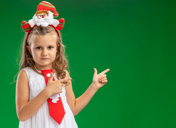 箍看起来小女孩戴着圣诞发箍和领带点在后面孤立的绿色墙壁与复制空间小领带圣诞节
