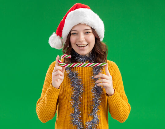 花环快乐的年轻斯拉夫女孩戴着圣诞帽 脖子上戴着花环 手里拿着糖果手杖举行空间绿色
