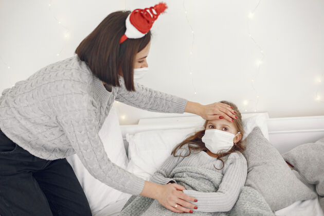 流感儿童中有冠状病毒母亲带着女儿孩子躺在床上戴着医用口罩的妇女流感母亲发烧