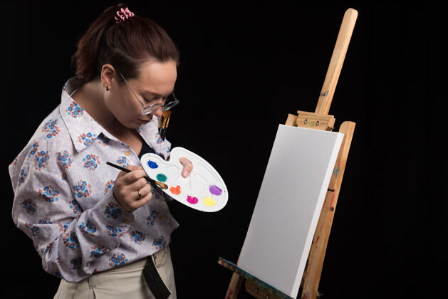 成人女画家用铅笔在画布上画一幅画 背景是黑色的艺术艺术家艺术品