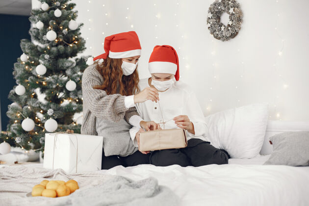母亲为圣诞节做准备的人冠状病毒主题妈妈和儿子玩穿白毛衣的男孩装饰圣诞节毛衣