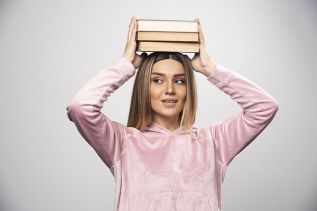 摆姿势一个穿着粉红色衬衫的女孩 头上抱着书年轻人女性学习