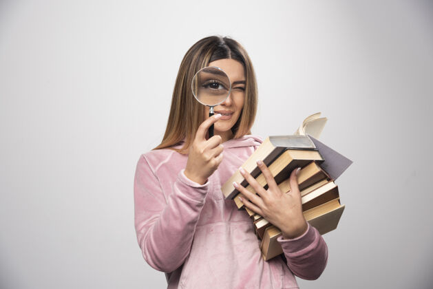 年轻人一个穿着粉色衬衫的女孩手里拿着一堆书 正试着用放大镜看上面的书呢携带成人放大镜