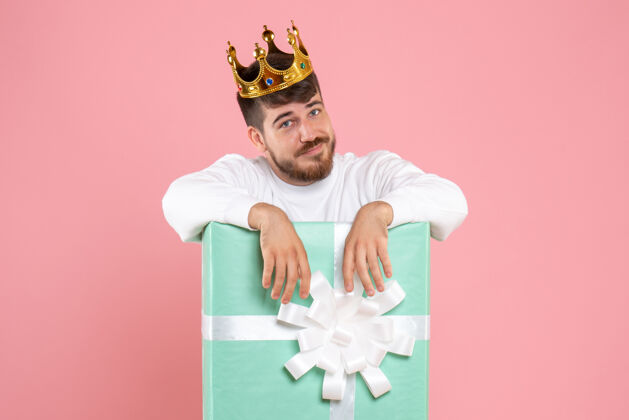成人年轻人在礼物盒内的正面视图 粉红色墙上有皇冠人物快乐男性