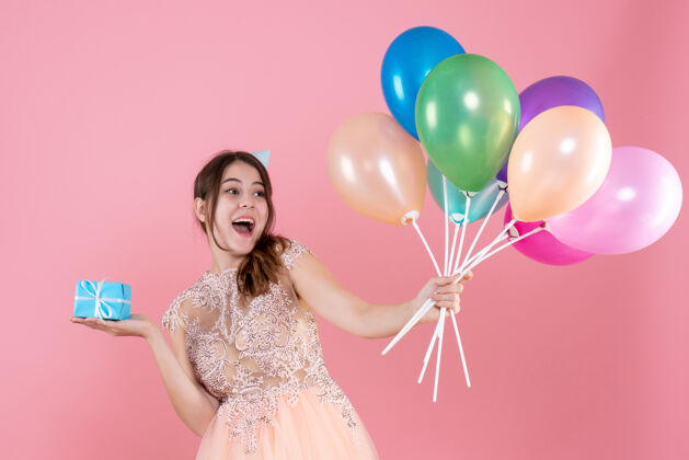 气球戴着派对帽的快乐女孩手里拿着五颜六色的气球和粉色的礼物帽子粉色气球