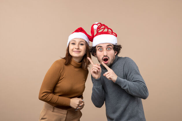 圣诞节日喜庆和聚会的概念-快乐可爱的年轻夫妇穿着灰色的镜头团结对方圣诞老人帽震惊肖像节日年轻