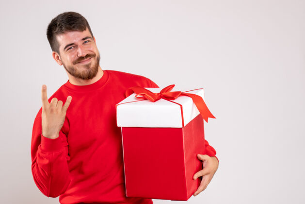 盒子身穿红衫的年轻人在白色墙上的盒子里拿着圣诞礼物的正视图惊喜圣诞节举行