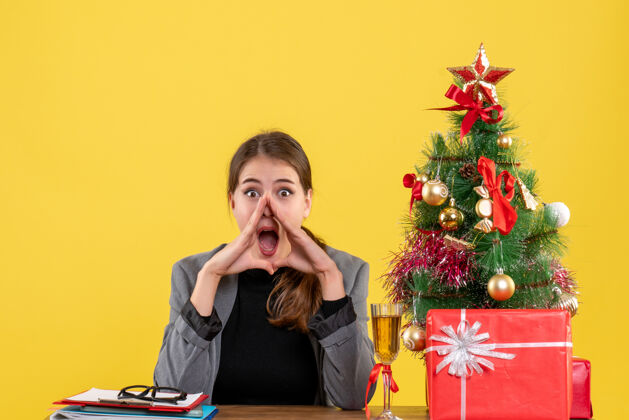 鸡尾酒前视图惊讶的女孩坐在圣诞树和礼物鸡尾酒附近的桌子惊喜微笑圣诞节